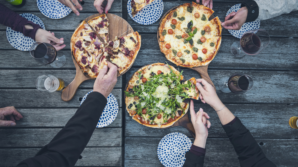 Hands reaching for stone baked pizza - a firm favourite on the menu at the Boatshed Cafe and Bar on the jetty at Punga Cove.