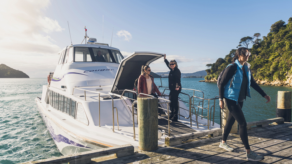 Two walkers disembarking from the Cougar Line boat at Ship Cove/Meretoto ready to walk on the Queen Charlotte Track.