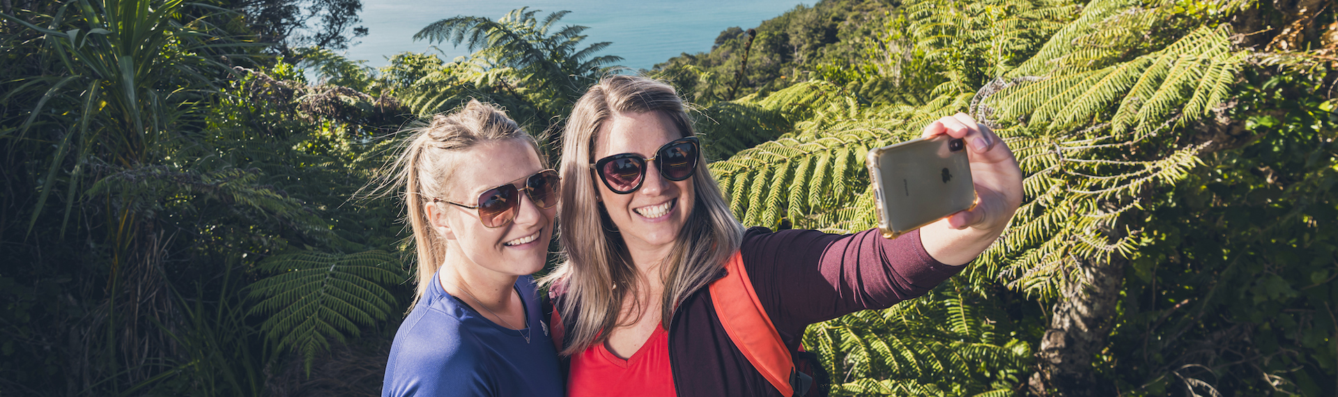 Two women take selfies at the lookout with Motuara Island in the background on the Queen Charlotte Track.