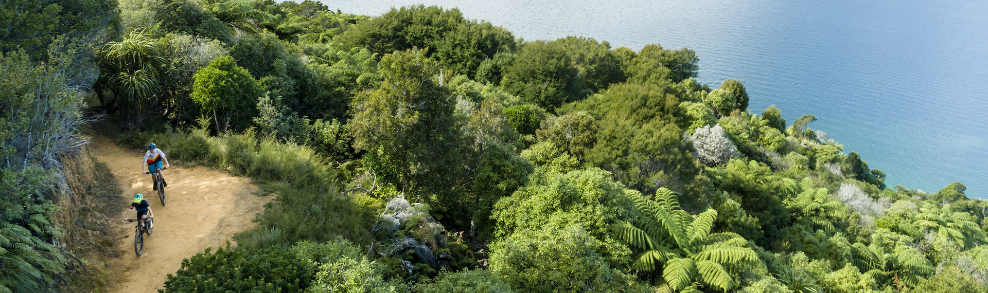 Aerial shot of two boys biking along the Queen Charlotte Track with Endeavour Inlet in the background.